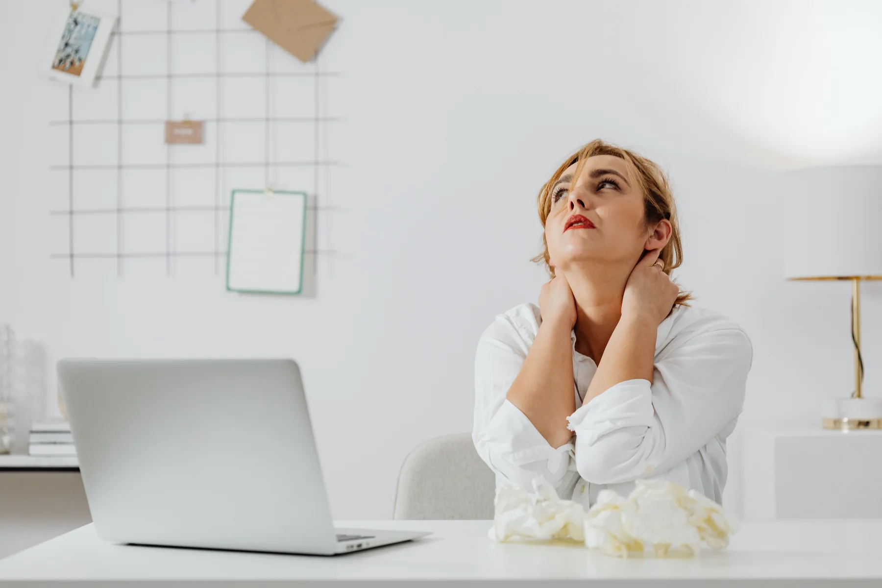 Real photo of a woman holding her neck while sitting at a laptop at work