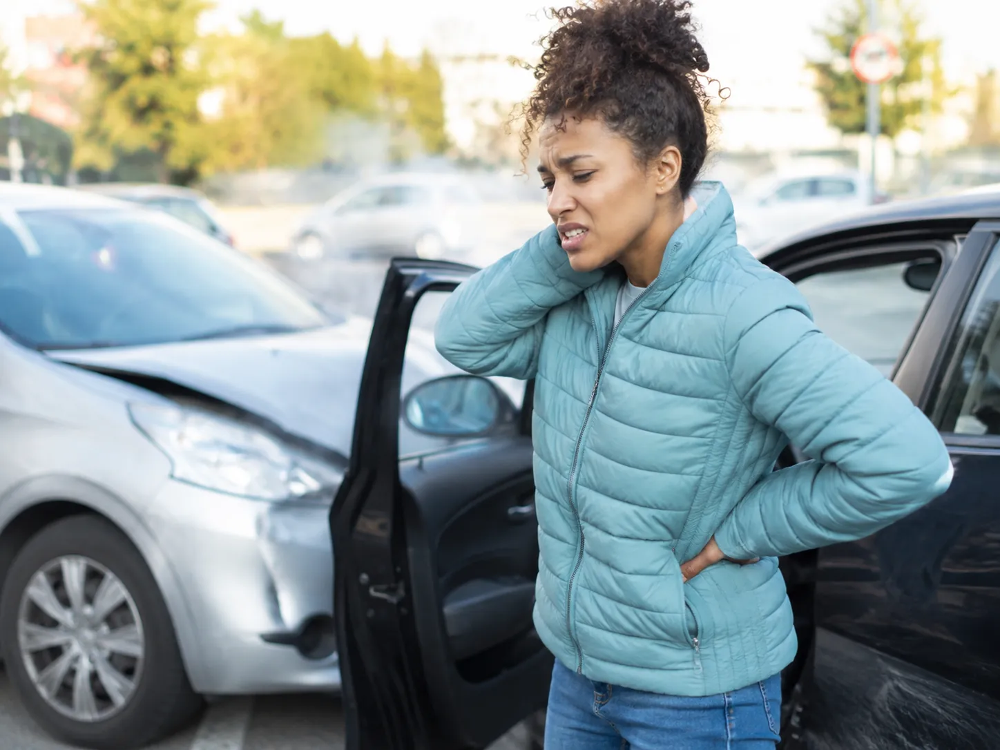 Woman holding her neck and lower back beside damaged vehicles after a car accident